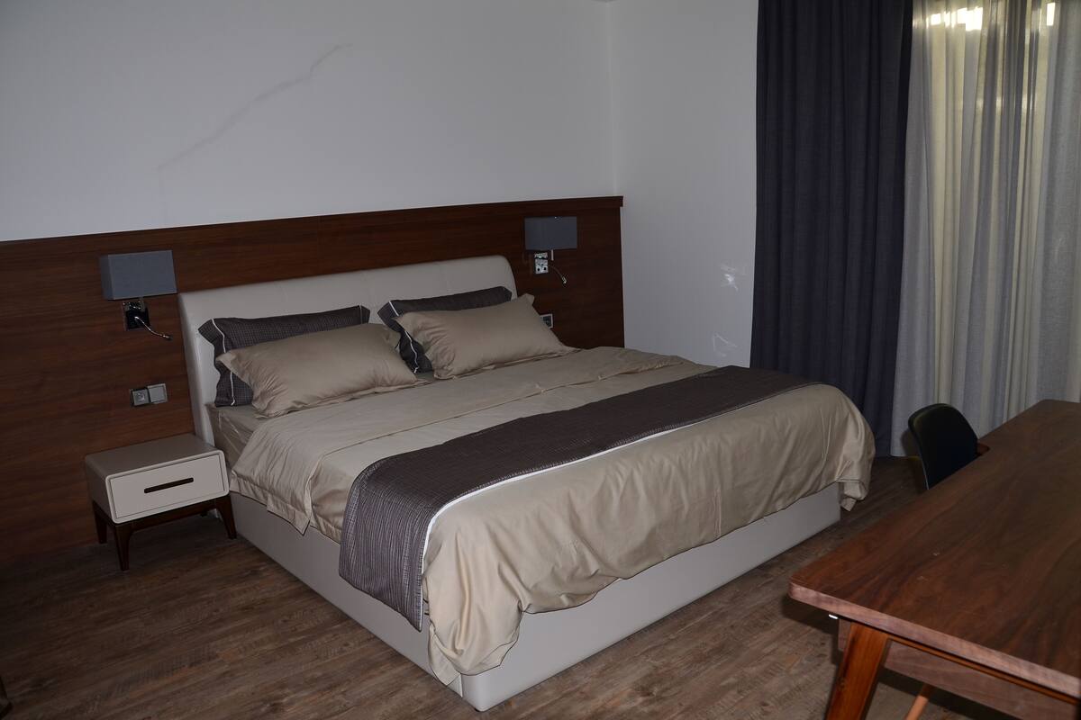 Una habitación de hotel con una cama grande, mesitas de noche, cabecera de madera y una mesa de madera.