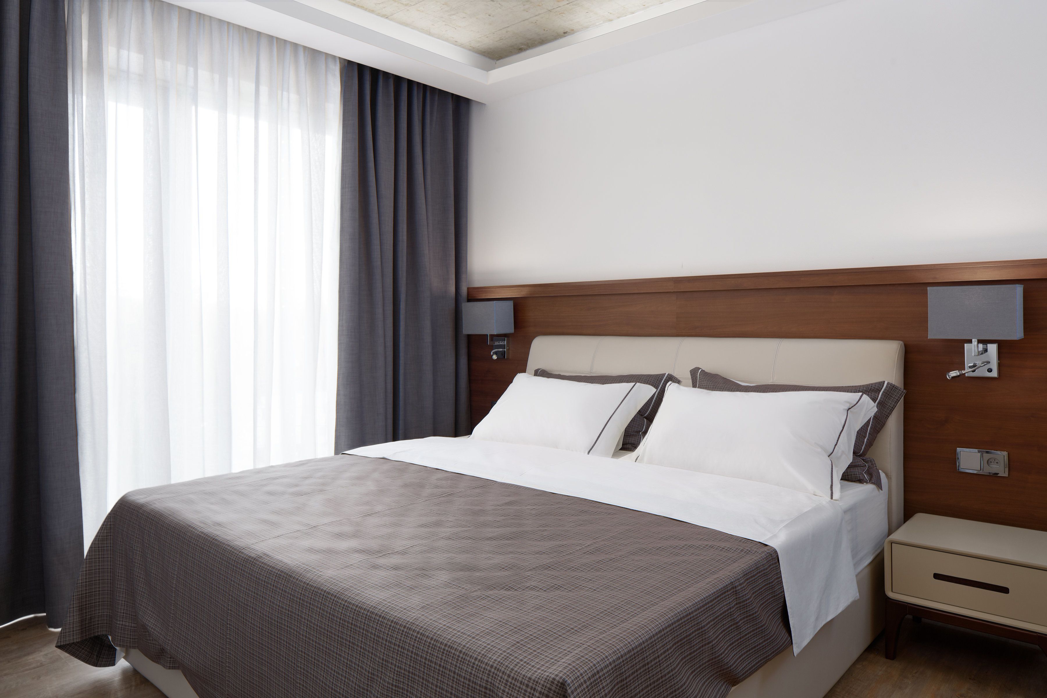 A hotel room with a large bed, a wooden headboard, a bedside table, and a nightstand.