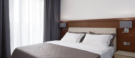 A hotel room with a large bed, a wooden headboard, a bedside table, and a nightstand.