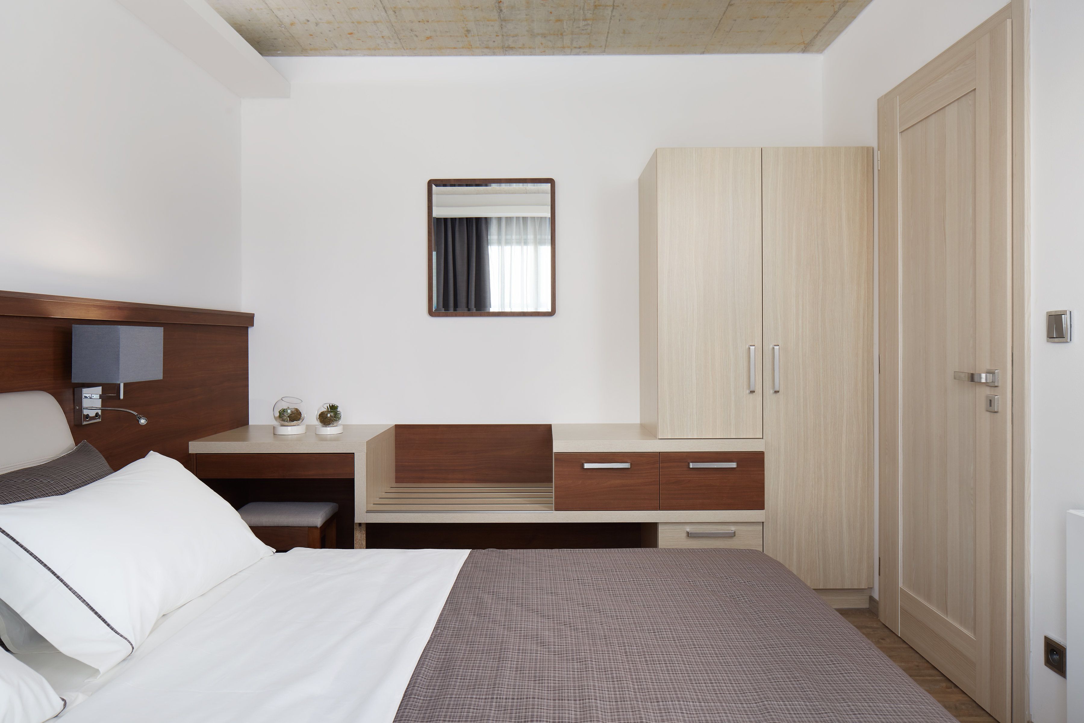 A hotel room with a bed, a desk, a wardrobe, and a mirror.