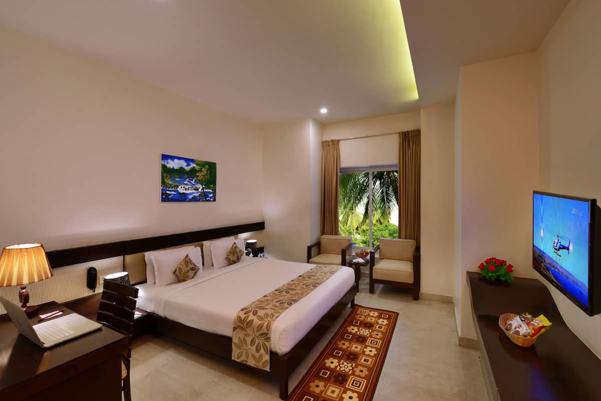 Quarto de hotel com cama, escrivaninha, cadeira, televisão e janela com cortinas.