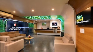 A hotel lobby with a reception desk, two sofas, a small table with flowers, and a TV screen displaying 'Rice bowl Vegetarian Restaurant'.