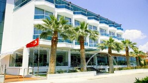 A modern hotel with a white facade, multiple floors, and a covered entrance with palm trees. - Idahan Hotel (Burhaniye)