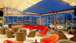 A rooftop restaurant with a glass enclosure, offering a view of the cityscape at night. - Idahan Hotel (Burhaniye)