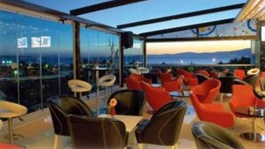 An outdoor seating area with modern chairs and tables, large windows offering a view of the cityscape and mountains. - Idahan Hotel (Burhaniye)