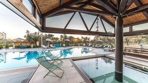 Una piscina interior moderna con paredes de vidrio transparente, sillas de descanso y sombrillas.