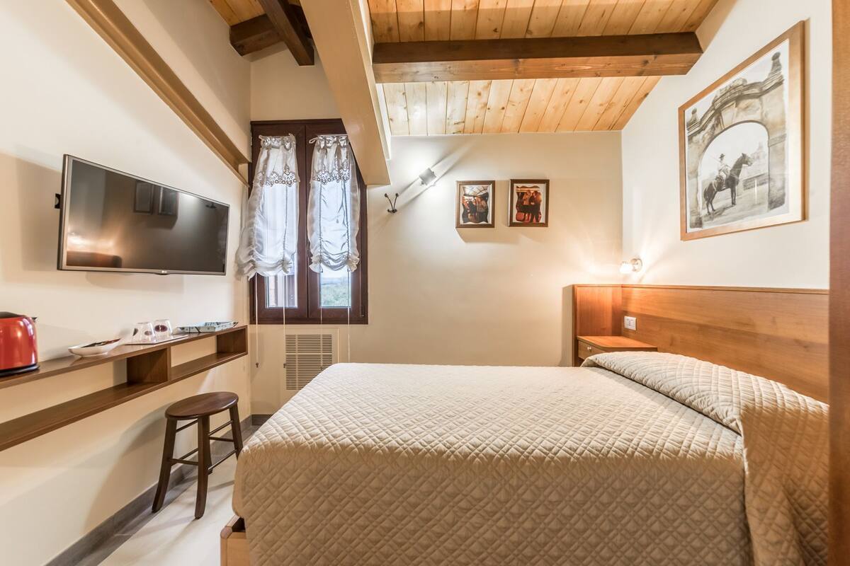 A bedroom with a bed, a TV, a desk, and a window with curtains.