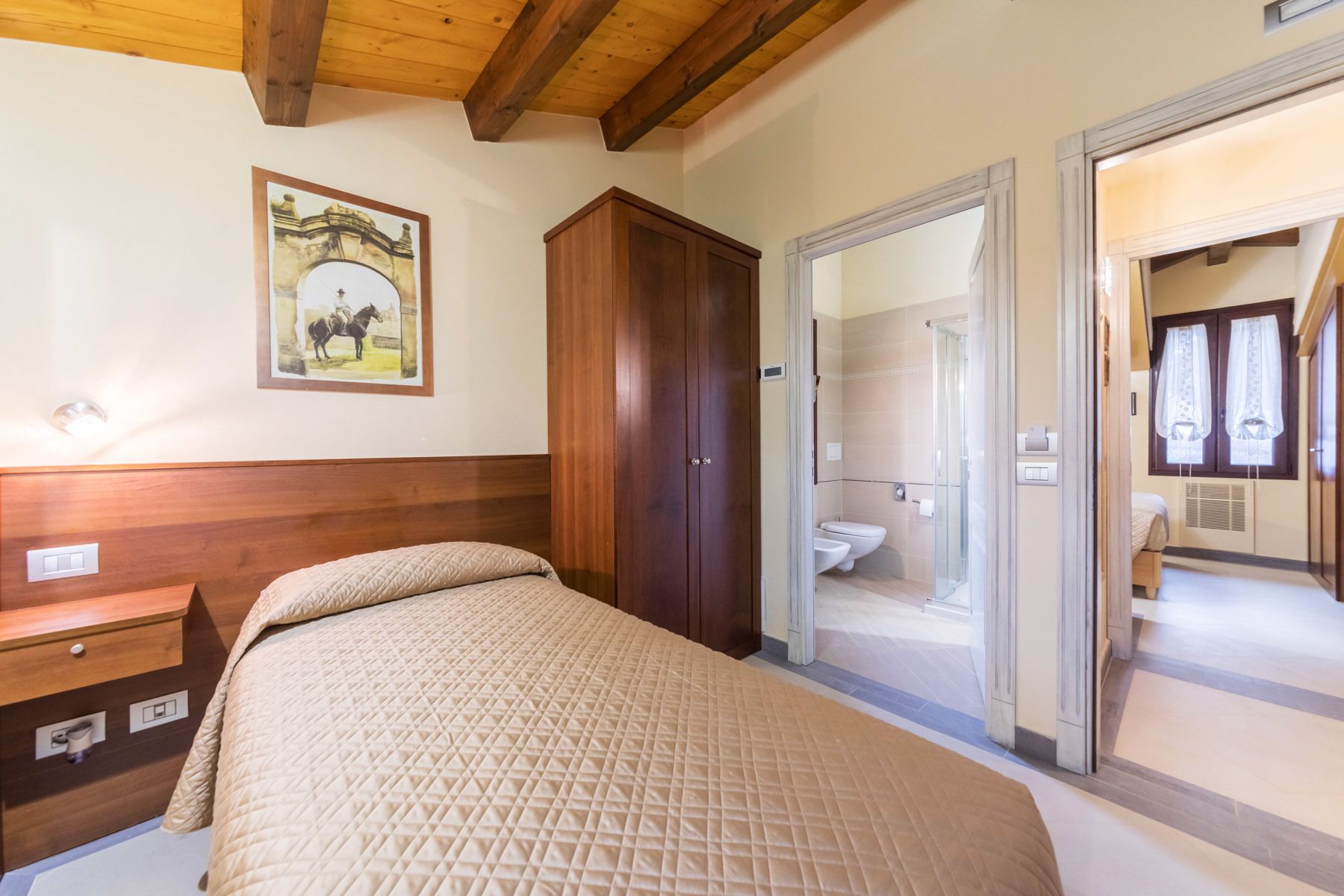 A bedroom with a bed, wooden wardrobe, and a bathroom with a shower and toilet.