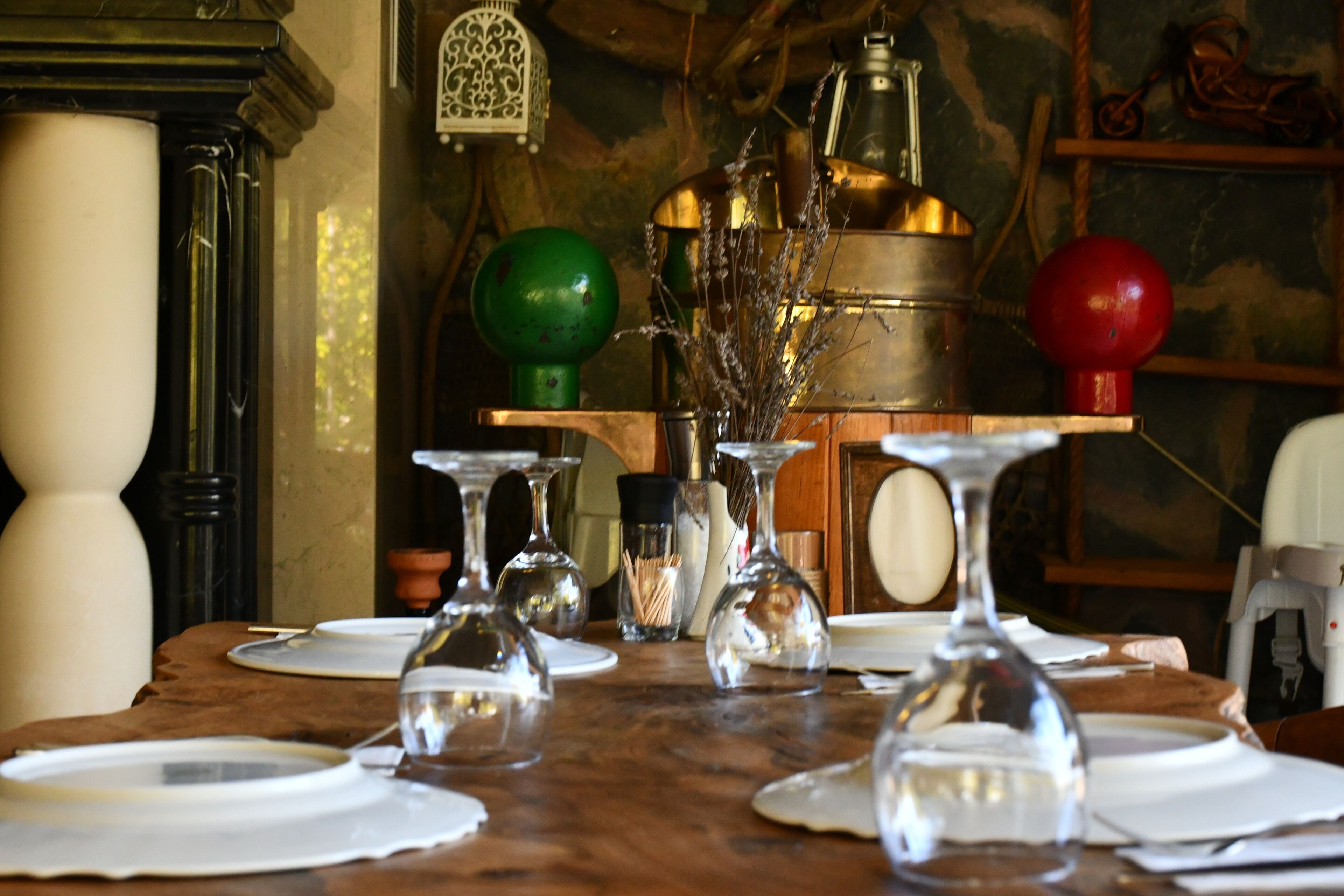 A dining table set with clear glassware and plates, surrounded by various decorative items and a vintage-style lamp.