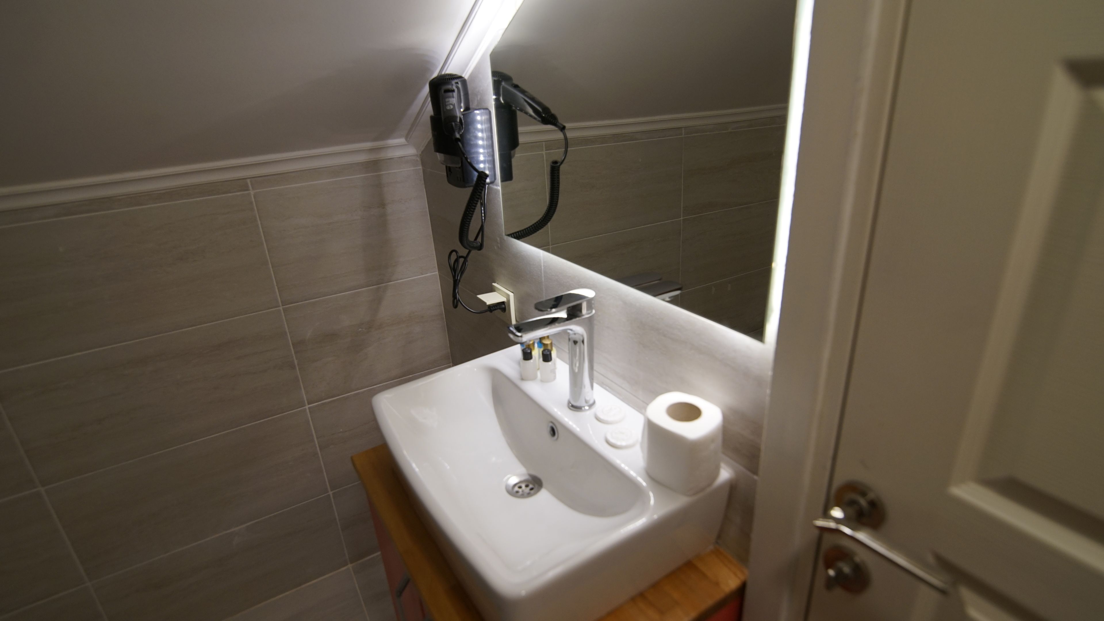 A bathroom with a white sink, a mirror, and a hairdryer on the wall.