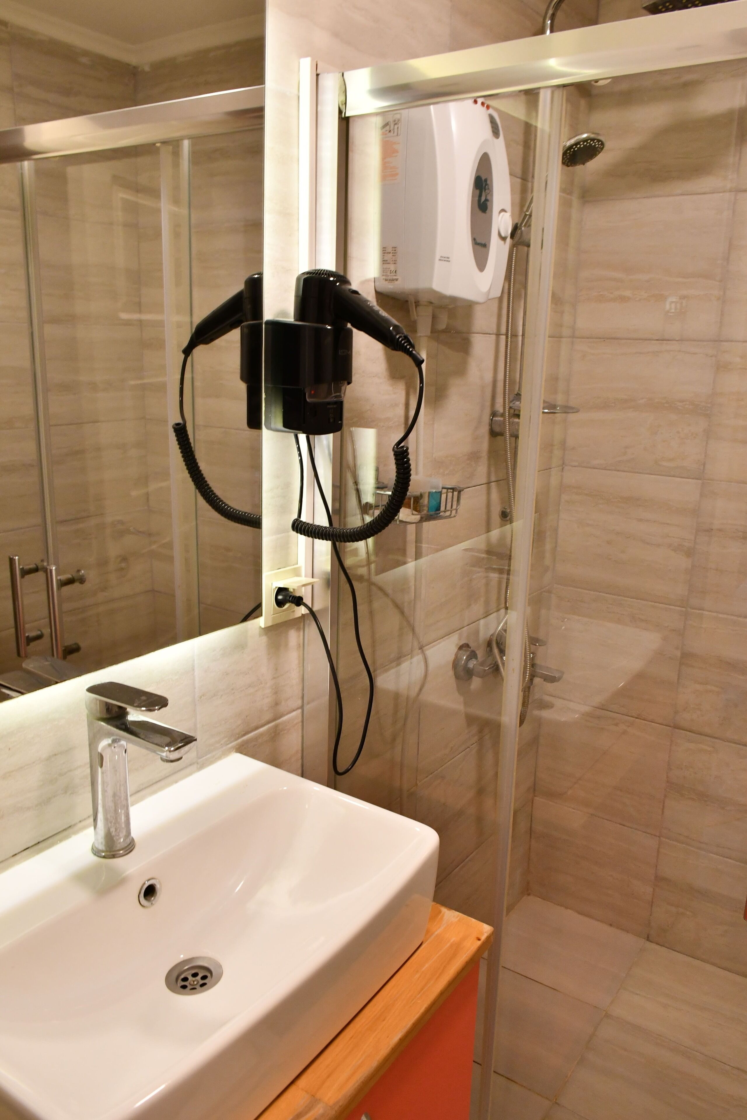 Un baño con lavamanos blanco, cabina de ducha con vidrio y un secador de pelo fijado en la pared.
