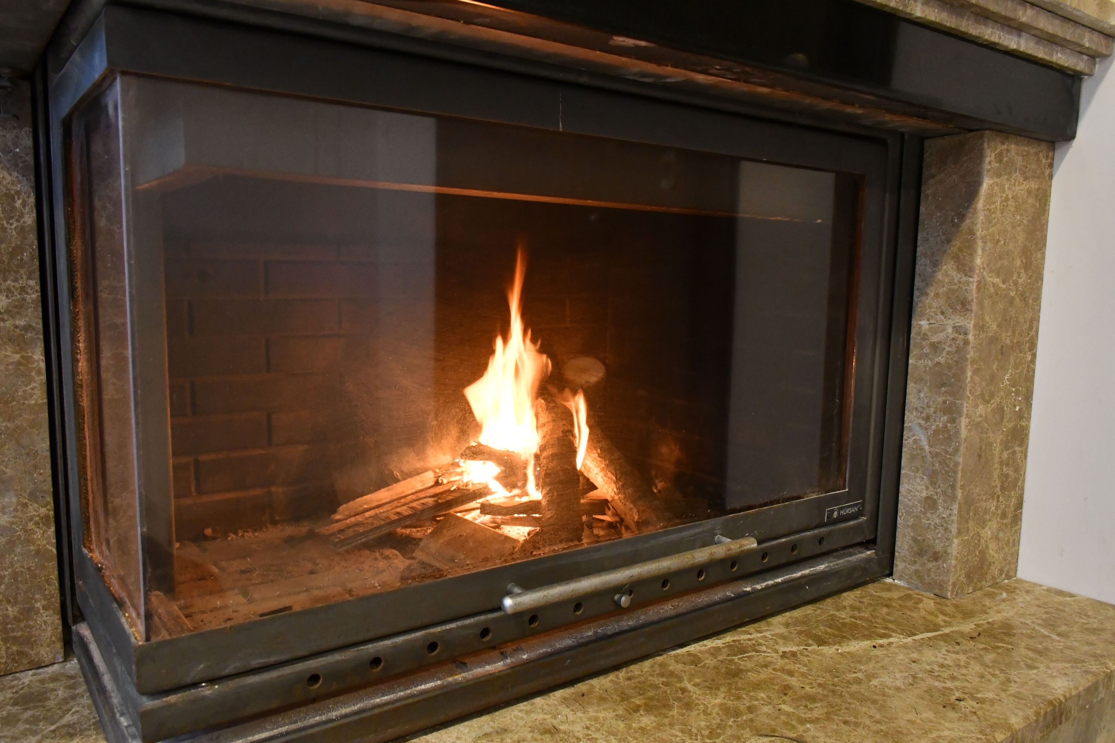 A fireplace with a glass front, a brick interior, and a metal frame.