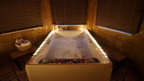 A large bathtub with rose petals, a basket of towels, and a wooden bench.