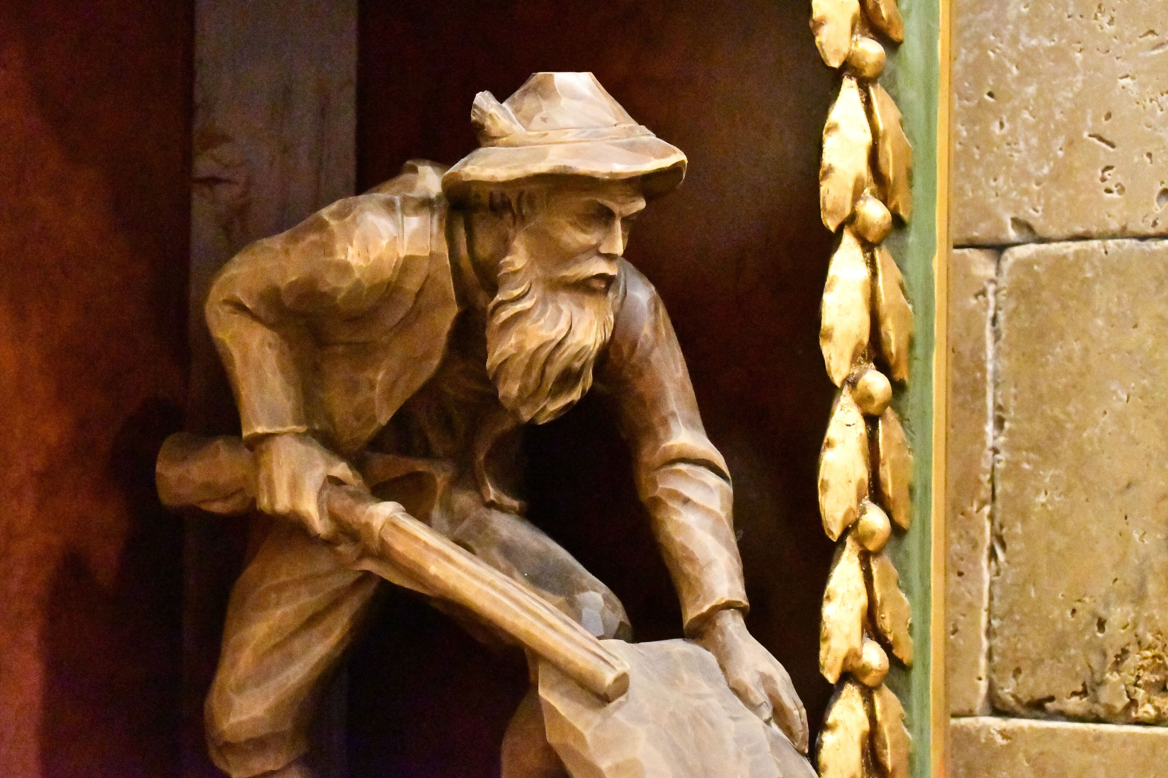 A wooden sculpture of a man with a beard, wearing a hat, and holding a shovel.