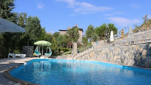 A swimming pool with a stone wall, lounge chairs, and umbrellas.