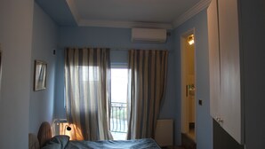 Un dormitorio con cama, unidad de aire acondicionado, ventana con cortinas, lámpara de noche y puerta que da a un baño.