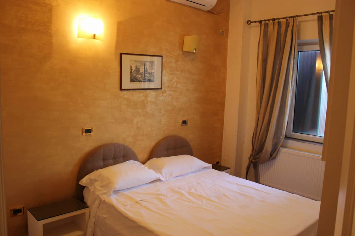 A bedroom with a bed, nightstands, a wall-mounted light, a picture, and a window with curtains.