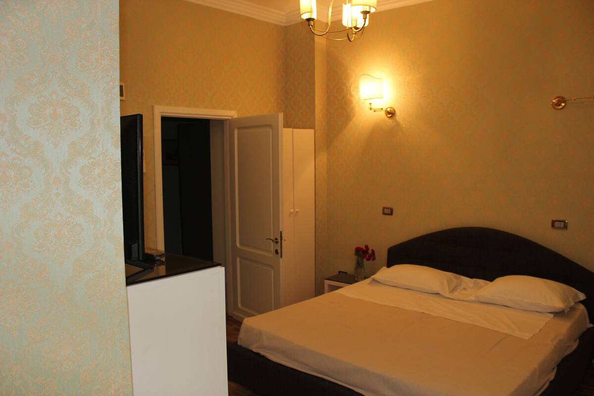 A hotel room with a bed, a nightstand, a mirror, and a door.