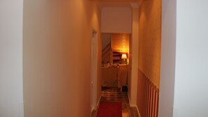 Un pasillo estrecho con una alfombra roja que conduce a una habitación con cama y mesita de noche.