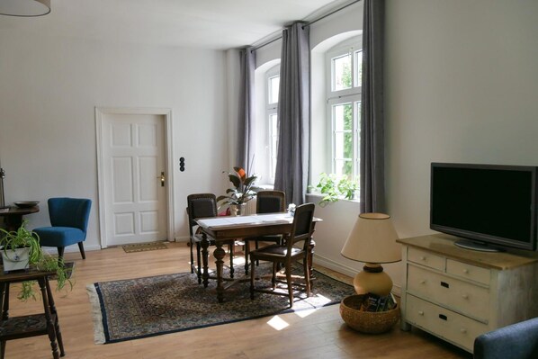 A living room with a dining table, chairs, a television, and a lamp.