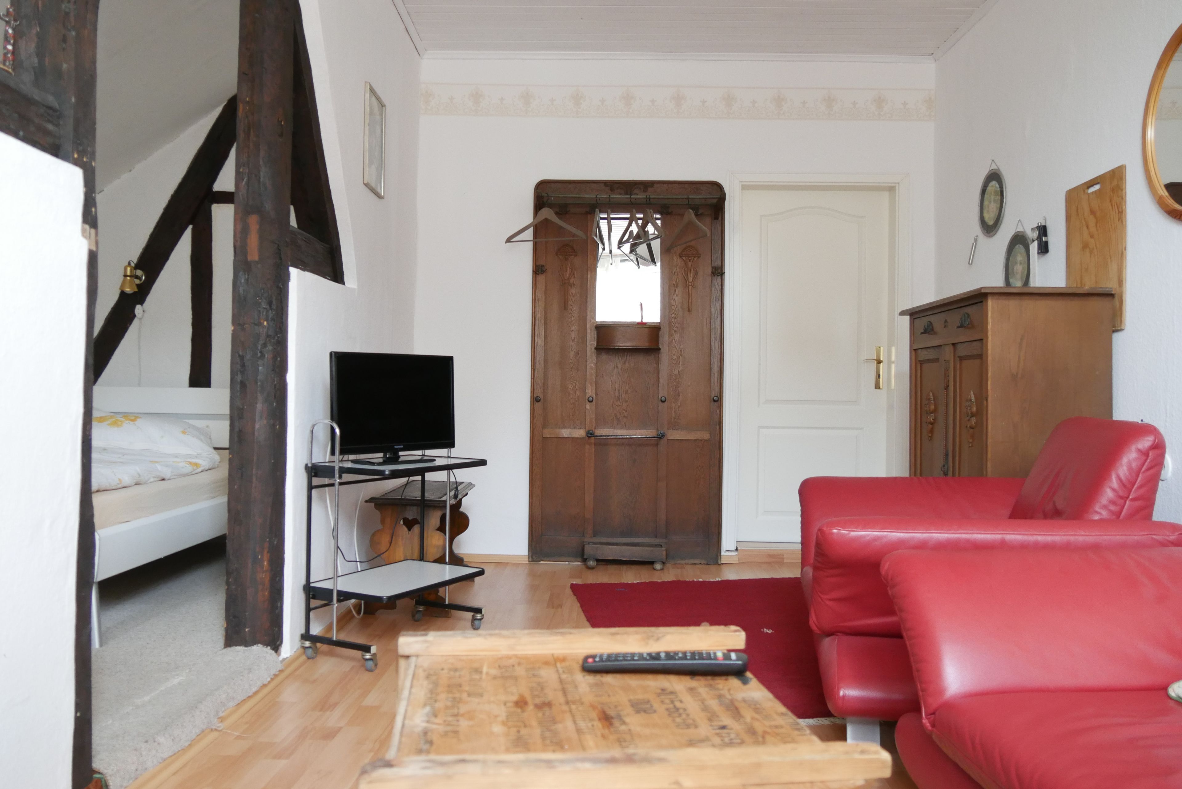 Une pièce avec un lit, un téléviseur posé sur un meuble, un canapé rouge et une table en bois avec une télécommande.
