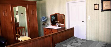 Un dormitorio con cama de madera, cómoda, espejo y puerta.