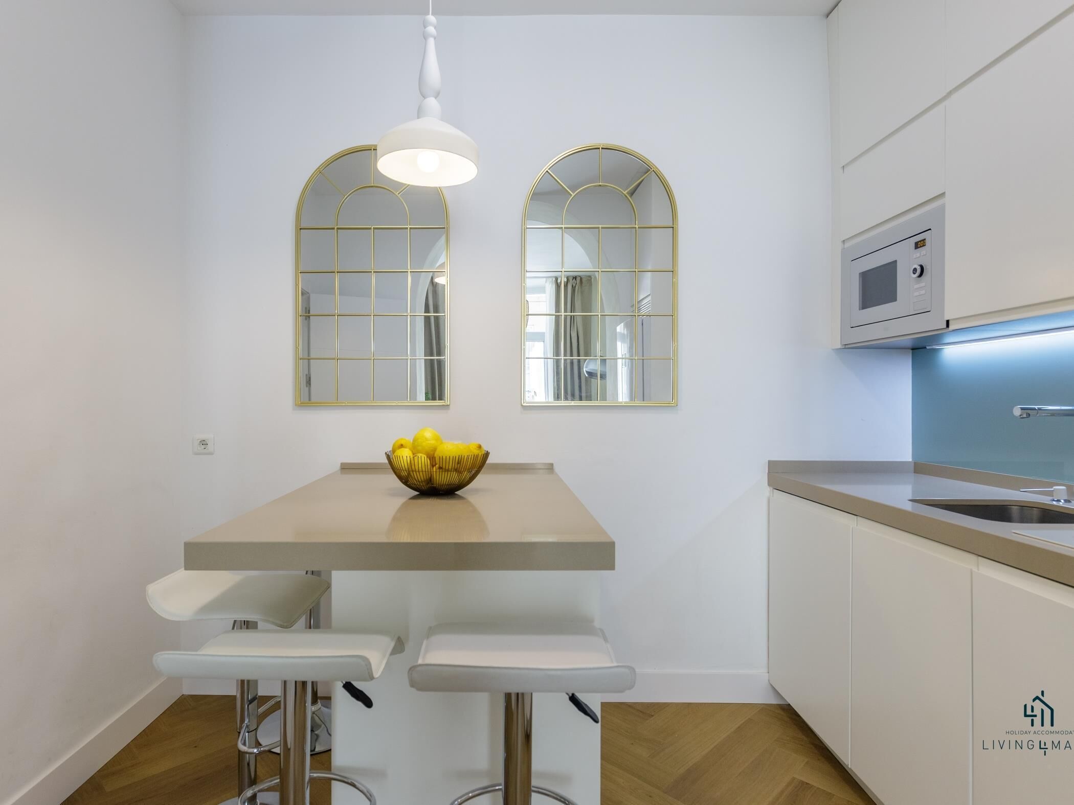 Una cocina moderna con encimera blanca, dos taburetes de bar, un cuenco de limones y dos espejos abovedados.