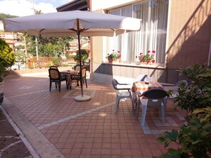 An outdoor patio with tiled flooring, a table with a checkered tablecloth, chairs, and a large umbrella. - Hotel Fleming (Fiuggi)