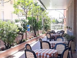 An outdoor patio with tables and chairs, surrounded by greenery and a fence. - Hotel Fleming (Fiuggi)