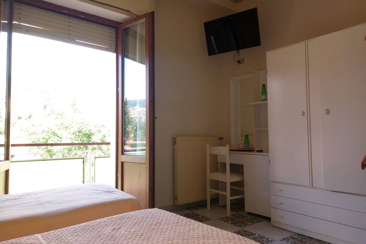A bedroom with a bed, a desk, a chair, a wardrobe, and a television.
