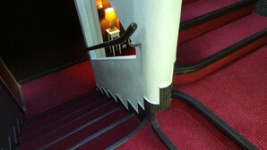 Una escalera con peldaños alfombrados de rojo y barandilla de metal.