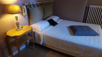 Una cama bien hecha con cubrecama acolchado, una mesita de noche con lámpara y una ventana con cortinas.