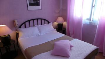 A neatly made bed with white and beige bedding, two bedside lamps, a telephone, and a framed picture on the wall.
