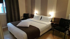 Una habitación de hotel con una cama grande, dos mesitas de noche, una silla y una ventana con cortinas.