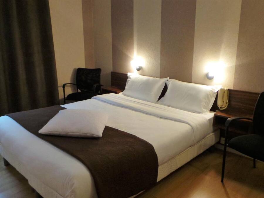 A hotel room with a large bed, two bedside tables, a chair, and a window with curtains.