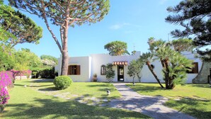 Un bâtiment blanc avec un toit recouvert de tuiles, entouré d’une pelouse bien entretenue et de divers arbres.