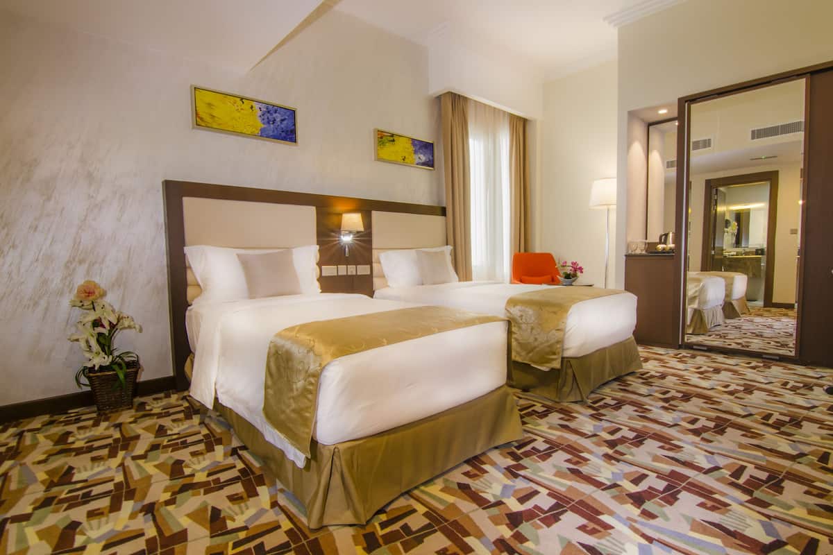 A hotel room with two beds, a large mirror, and a patterned carpet.