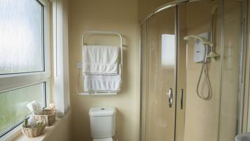 A bathroom with a toilet, a glass shower enclosure, and a window with a view.