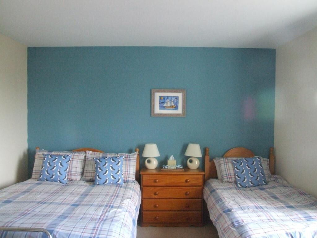 A room with two beds, each with a wooden headboard, a nightstand with two lamps, and a framed picture on the wall.