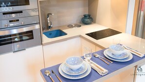 Una cocina moderna con electrodomésticos de acero inoxidable, un lavamanos azul y una zona de comedor con platos y cubiertos azules.