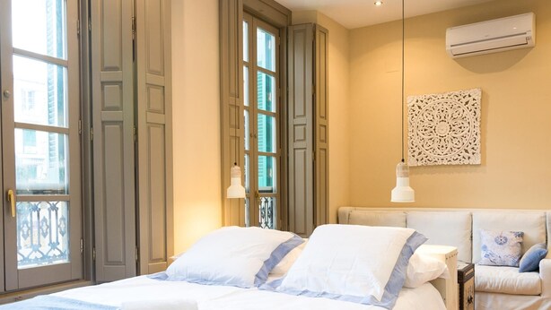 Un dormitorio con una cama grande, un sofá más pequeño, un adorno de pared y un equipo de aire acondicionado.