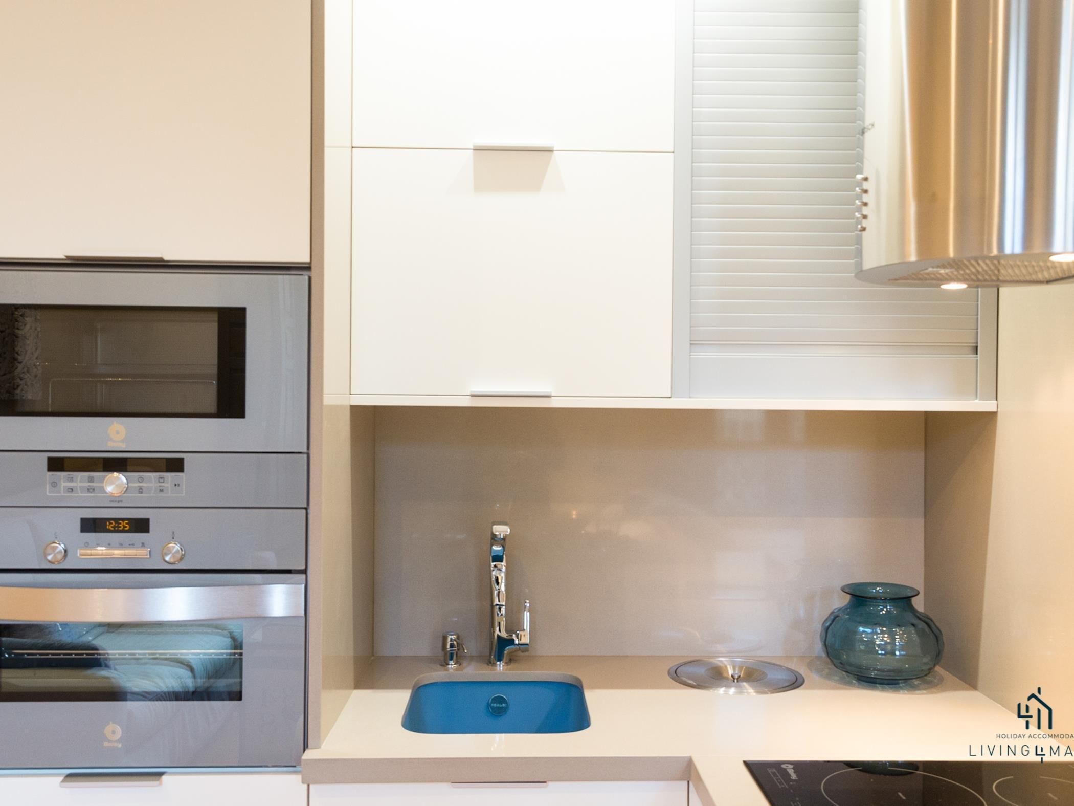 A modern kitchen with stainless steel appliances, a blue sink, and a decorative glass vase.