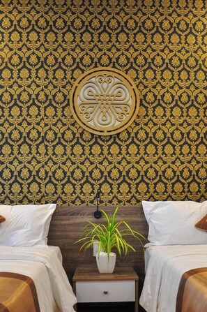 Habitación de hotel con papel tapiz estampado, un adorno de pared, dos camas, una mesita de noche con una planta y un cabecero de madera.
