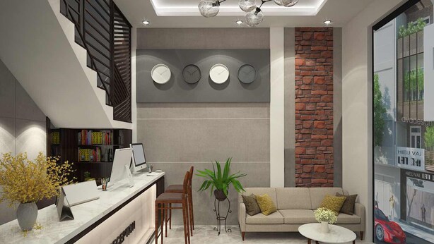A modern reception area with a desk, chairs, a sofa, and a coffee table. There are clocks on the wall, a plant, and a brick accent wall. - Nice Hue Hotel (Hue)