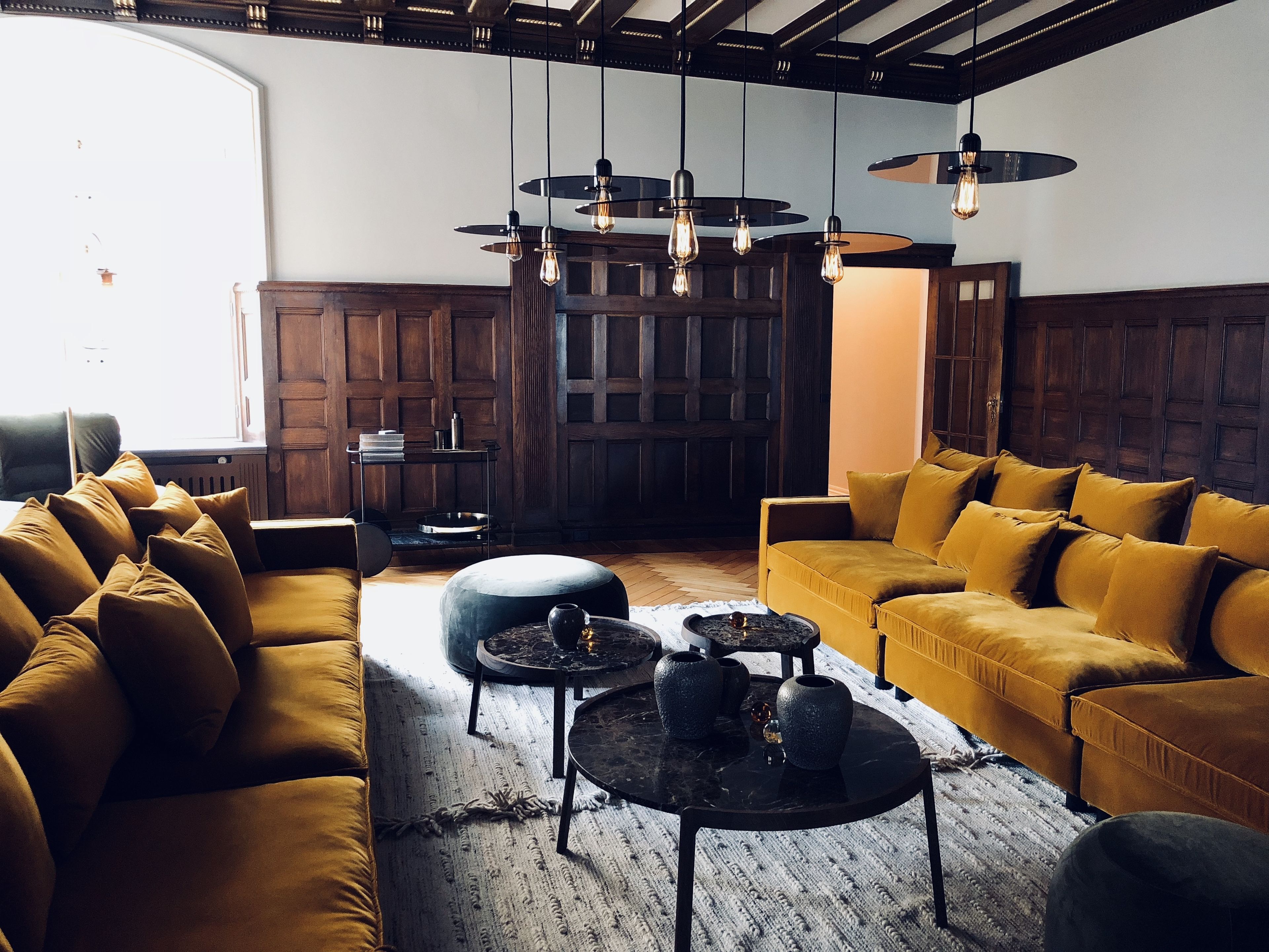 A modern living room with a large window, wooden paneling, and a yellow sofa set.