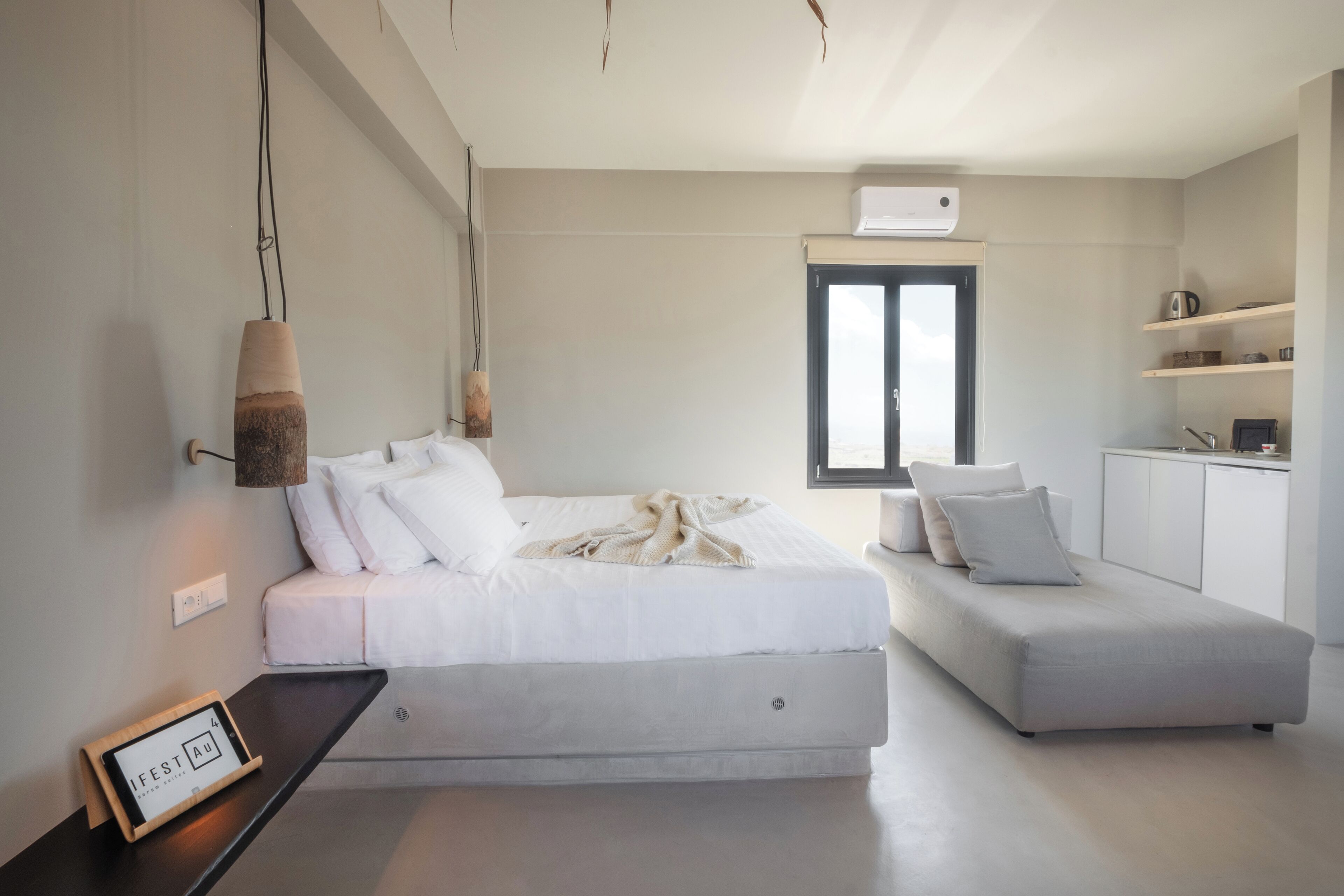 A modern bedroom with a bed, a daybed, a bedside table with a clock, and a window with blinds.