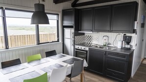 A modern kitchen with a large window, a dining table with chairs, and built-in appliances. - Black beach cottage (Sveitarfélagid Ölfus)
