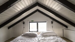 A room with a sloped ceiling, a bed with white bedding, and a window with a view. - Black beach cottage (Sveitarfélagid Ölfus)