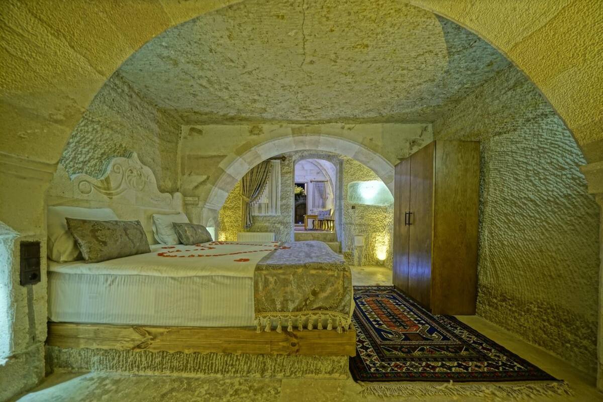 A stone-walled bedroom with a bed, pillows, a bench, and a patterned rug.