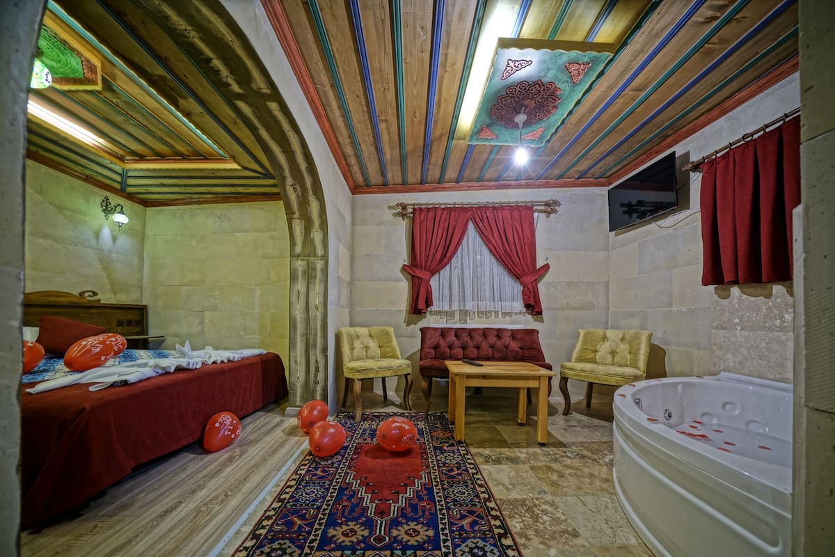 A room with a bed, two armchairs, a small table, a red rug, and a bathtub.